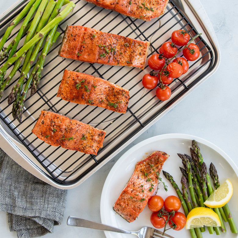 Stainless steel oven roasting pan with rack holding salmon asparagus and cherry tomatoes