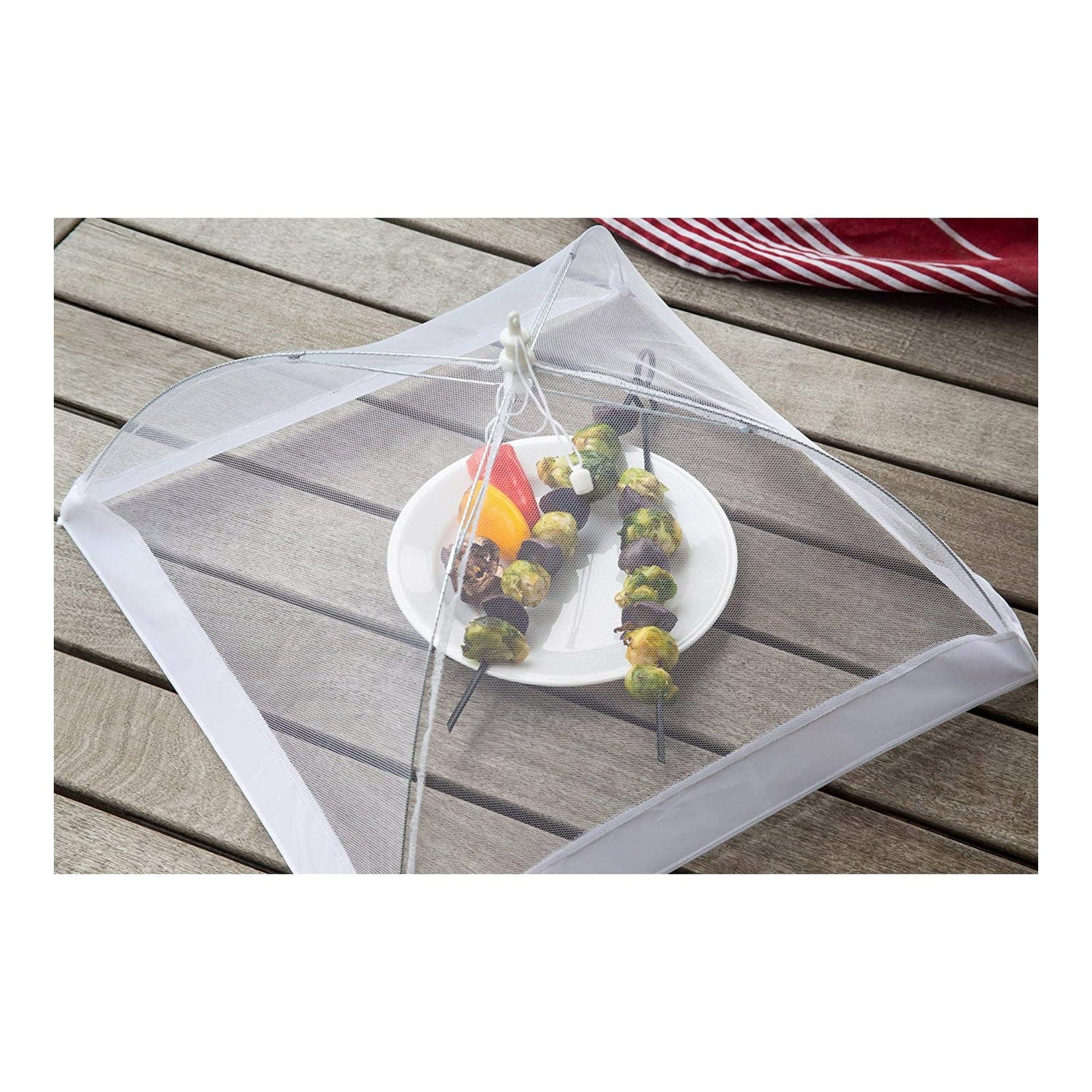 White square food umbrella made of mesh covering skewers and vegetables on a white plate