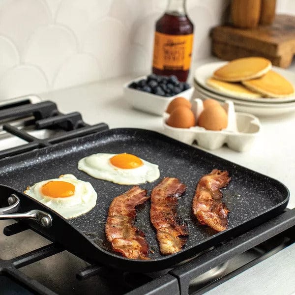 Nordic Ware Basalt 11 Square Griddle in black cooking eggs and bacon on a stovetop