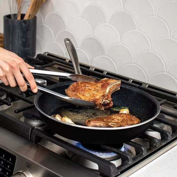 Nordic Ware Basalt 12 Saute Skillet in black cooking two pork chops on a gas stove