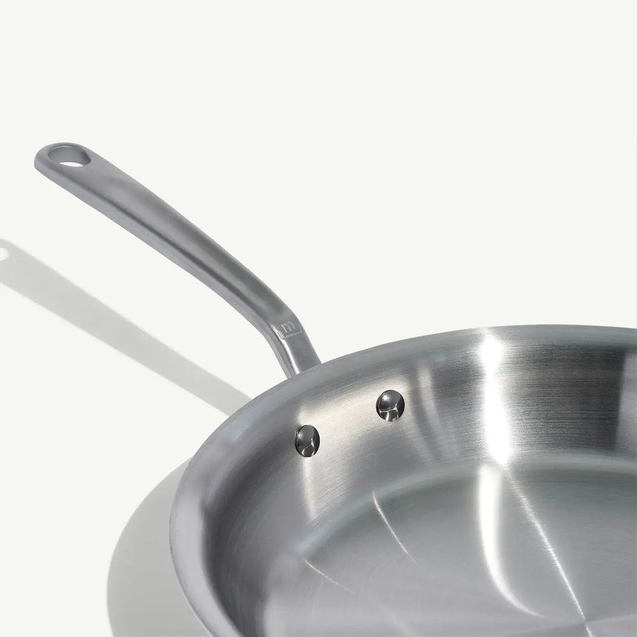 12 stainless clad frying pan with a long handle and riveted interior shown on a white surface