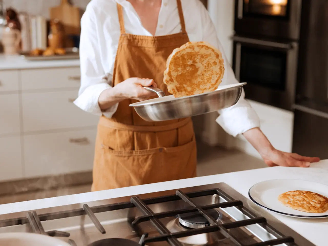 A person flipping a pancake in a stainless steel 8 CeramiClad frying pan