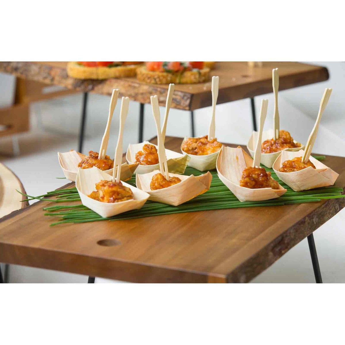 Light brown bamboo fork picks in a snack boat holding an appetizer on a wooden board