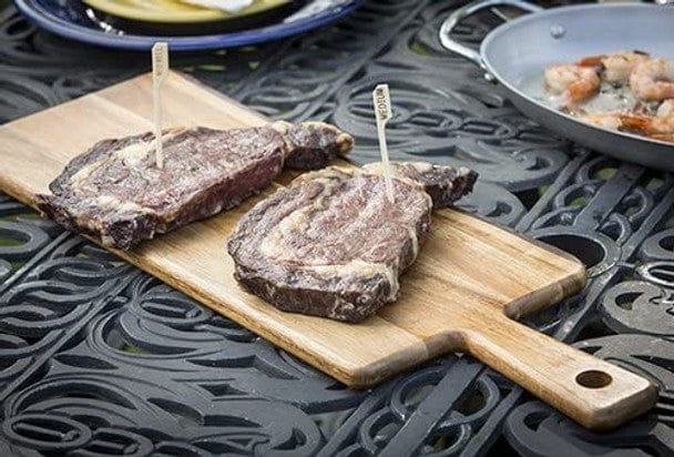 3 5 natural bamboo steak markers stuck in two steaks on a cutting board with MEDIUM visible on one marker