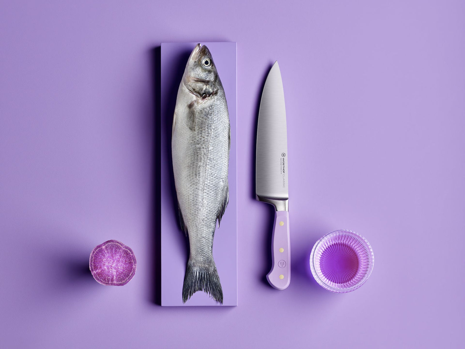 Lavender Wusthof Classic 8 Chefs Knife with a fish a half potato and a bowl of liquid on a purple surface