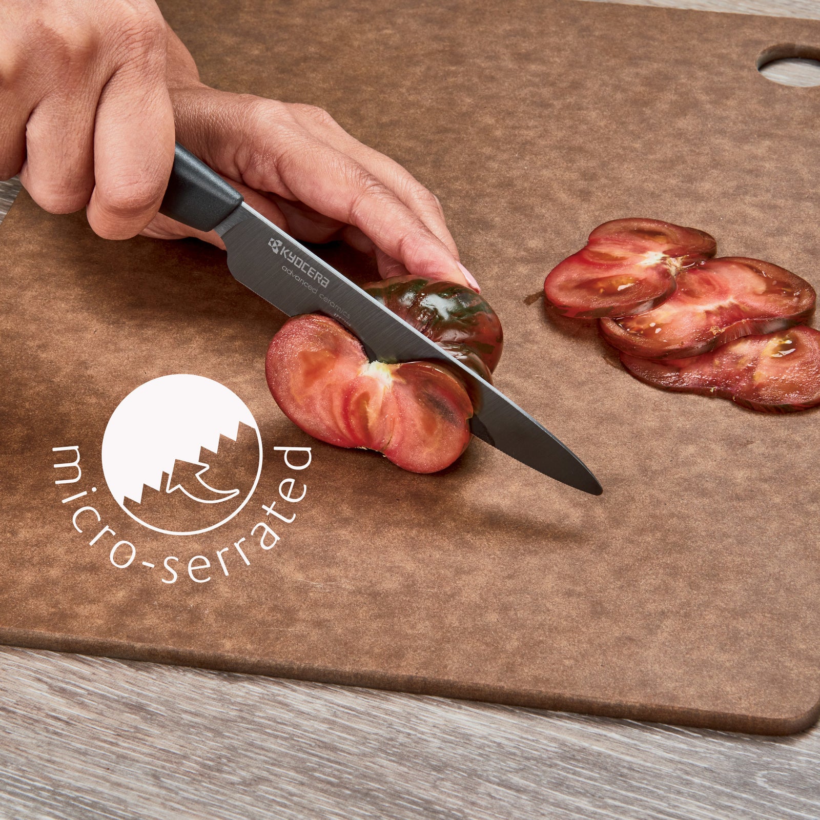 Hand slicing a tomato with a 5 Kyocera Revolution black ceramic micro serrated tomato knife with a gray handle