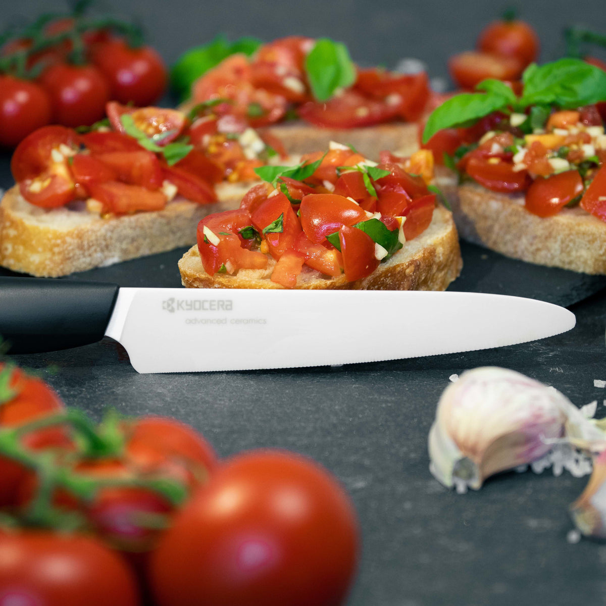 Kyocera Revolution 5 micro-serrated ceramic tomato knife with white blade and black handle near bruschetta