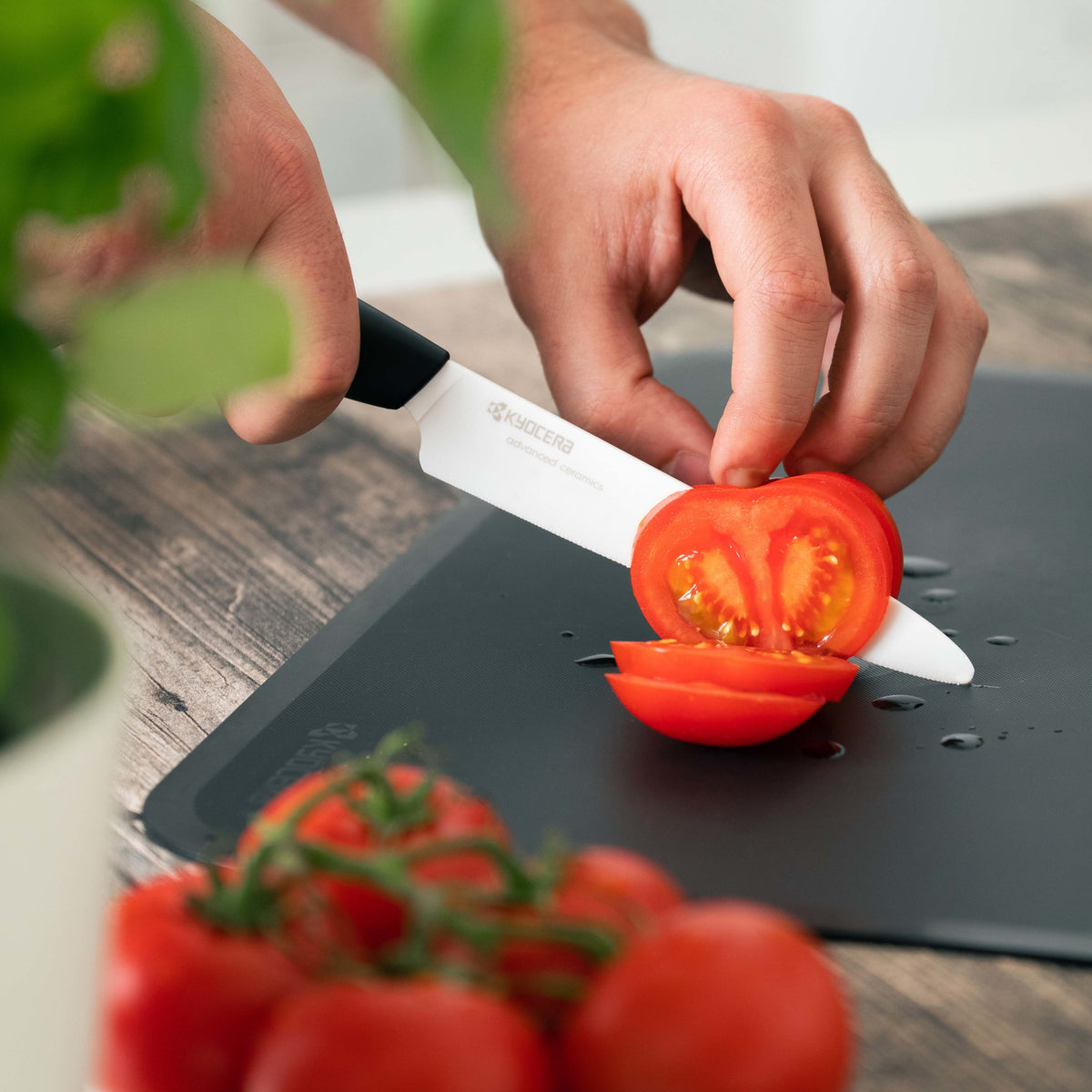 Hand slicing a red tomato with a Kyocera Revolution 5 ceramic tomato knife with a white blade and black handle