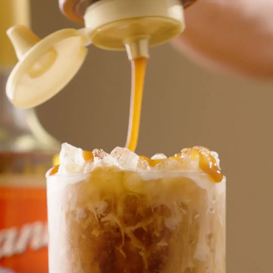 Caramel sauce pouring onto an iced coffee with whipped cream and ice in a clear glass
