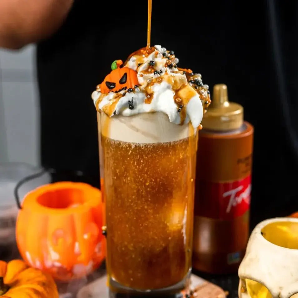 Tall glass of Halloween drink with whipped cream pumpkin candy sprinkles and caramel drizzle