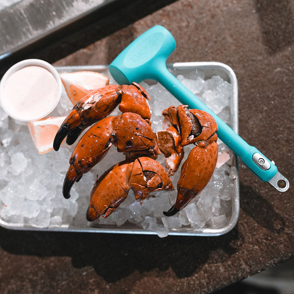 Aqua blue seafood mallet with a metal handle accent resting on a bed of ice with crab claws and dip