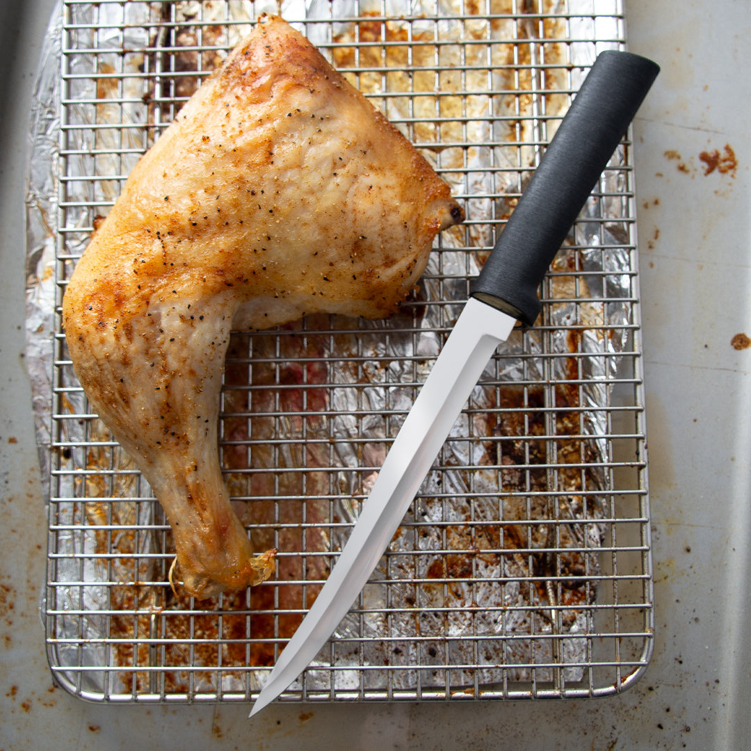 Steel boning knife with black handle next to roasted chicken leg on a metal cooling rack