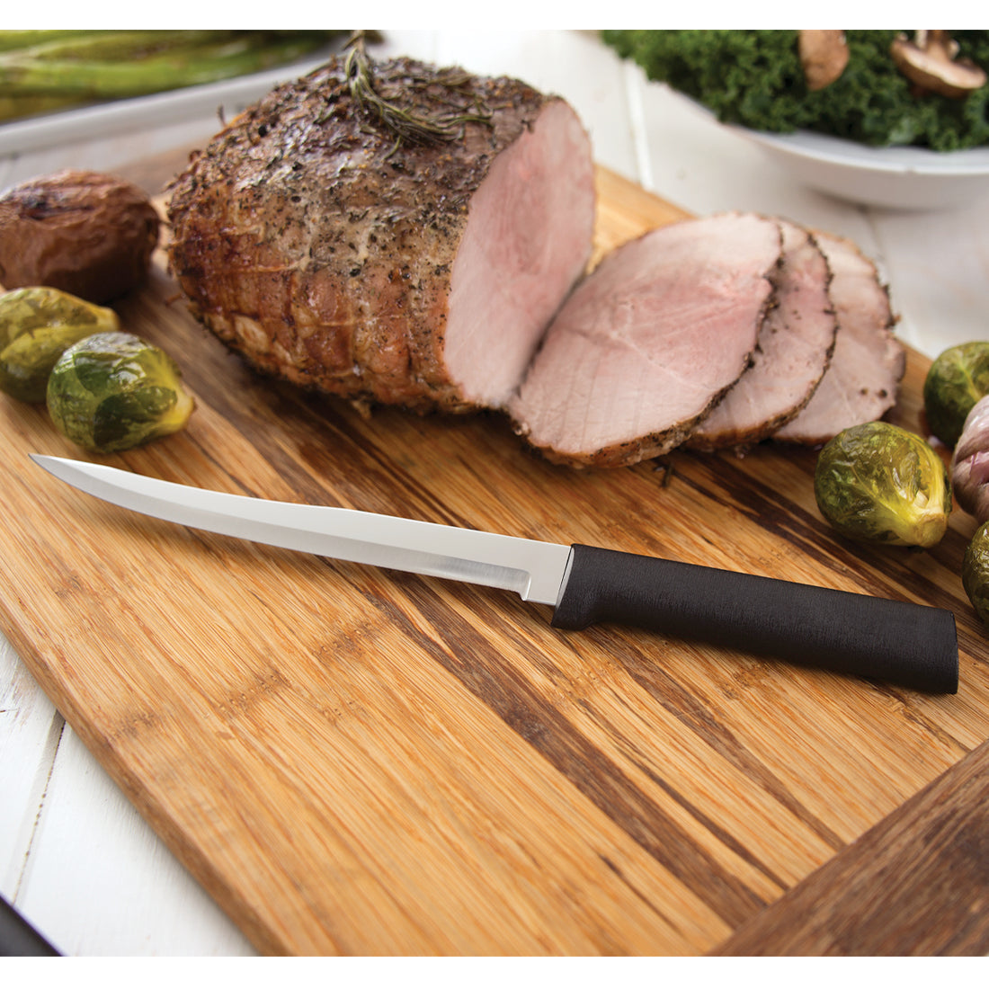 Stainless steel boning knife with black handle on a wooden cutting board with sliced roast and vegetables
