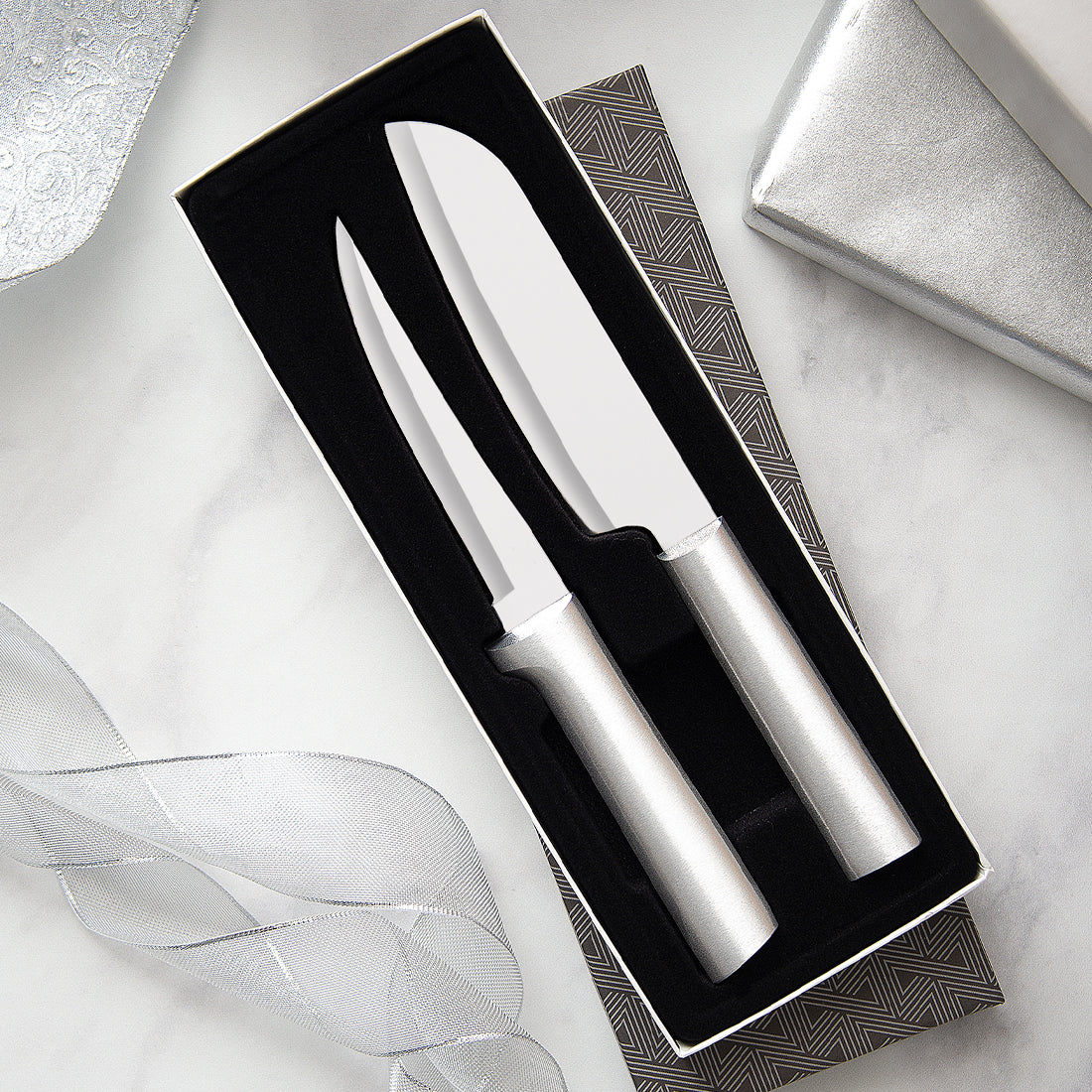 Two silver stainless steel carving knives with metallic handles in a black velvet gift box on a marble surface