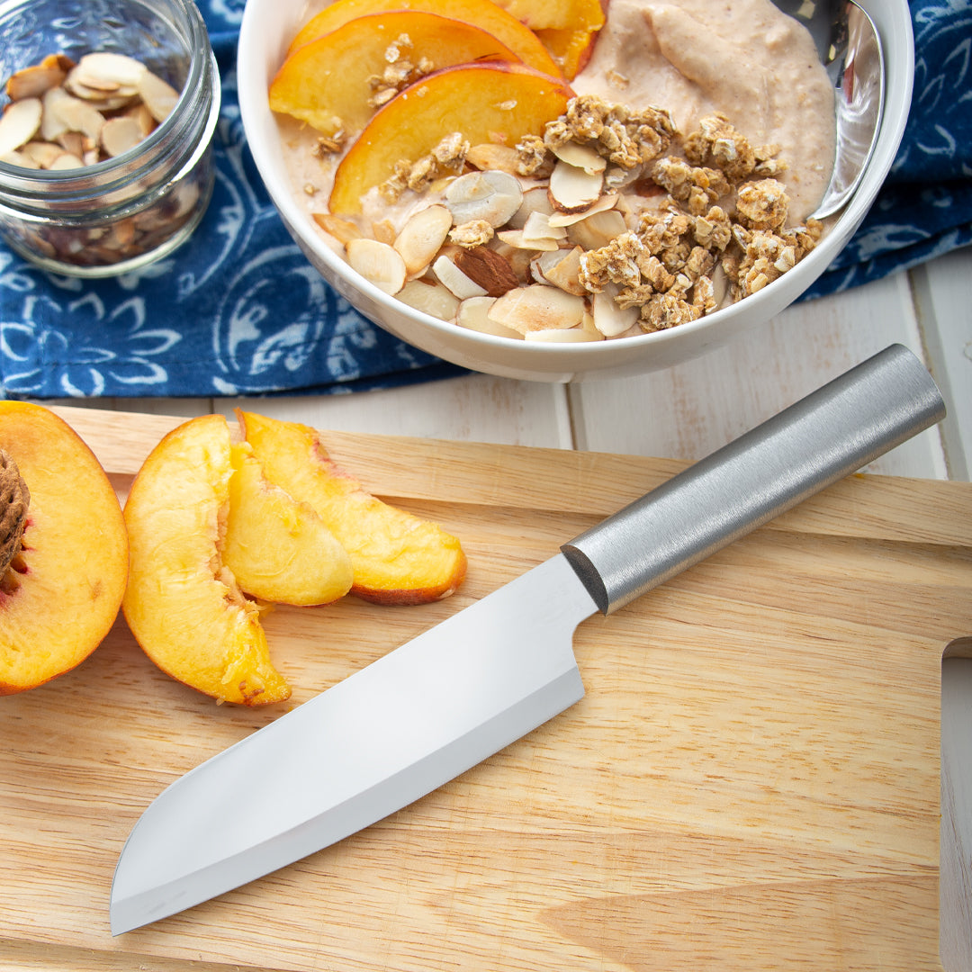 Stainless steel chefs knife on a light wooden cutting board with sliced peaches nearby