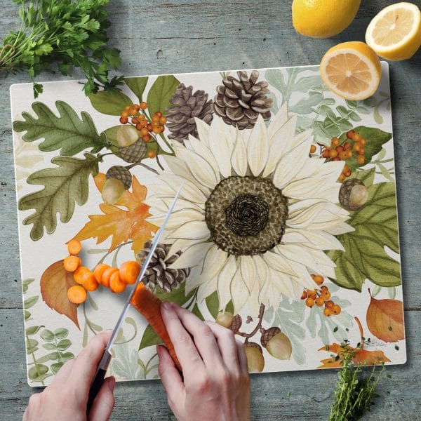 Glass cutting board with farmhouse fall design featuring a large cream sunflower acorns berries and autumn leaves