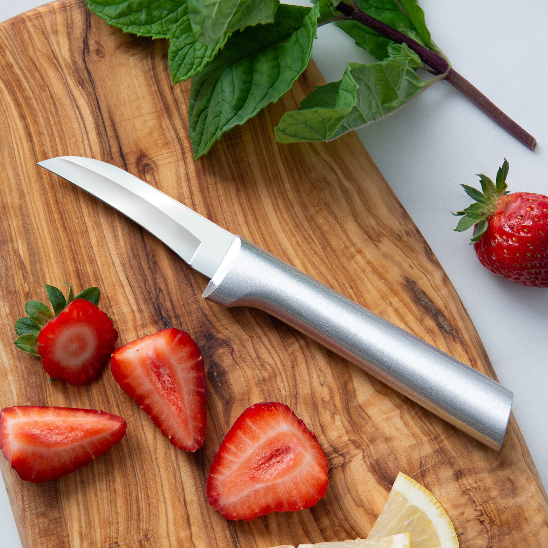 Silver-handled stainless steel paring knife on a wooden cutting board with sliced strawberries and mint