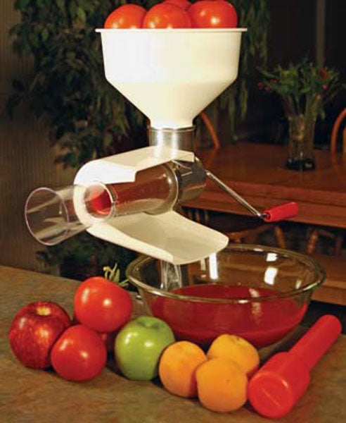 White manual food mill with a red handle and a clear bowl of sauce Whole fruits surround it