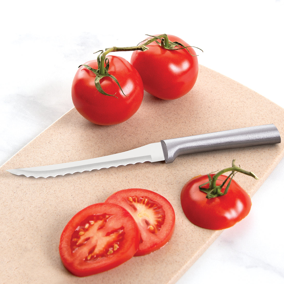 Silver-handled stainless steel serrated tomato knife on a beige cutting board with whole and sliced red tomatoes