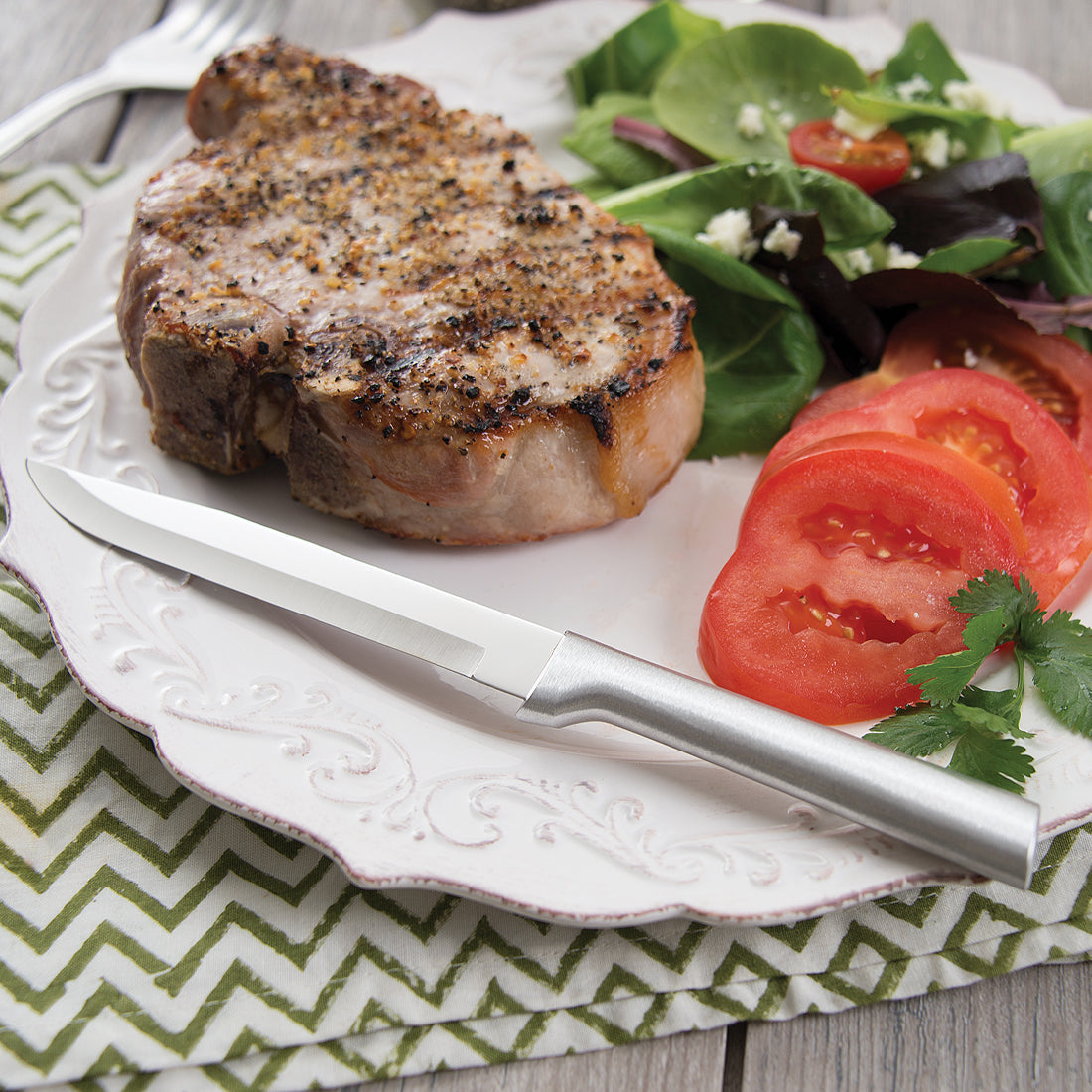 Stainless steel steak knife with a polished blade and a matte silver handle lying on a white dinner plate