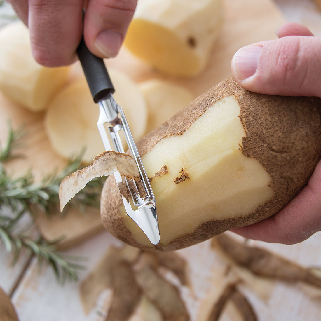 OXO Good Grips Swivel Peeler with a black handle and stainless steel blade peeling a potato