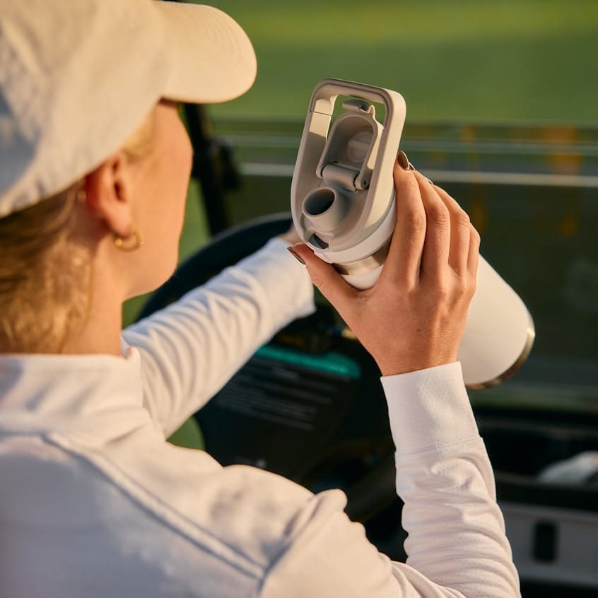 White stainless steel water bottle with a gray sipper lid held by a woman in a golf cart